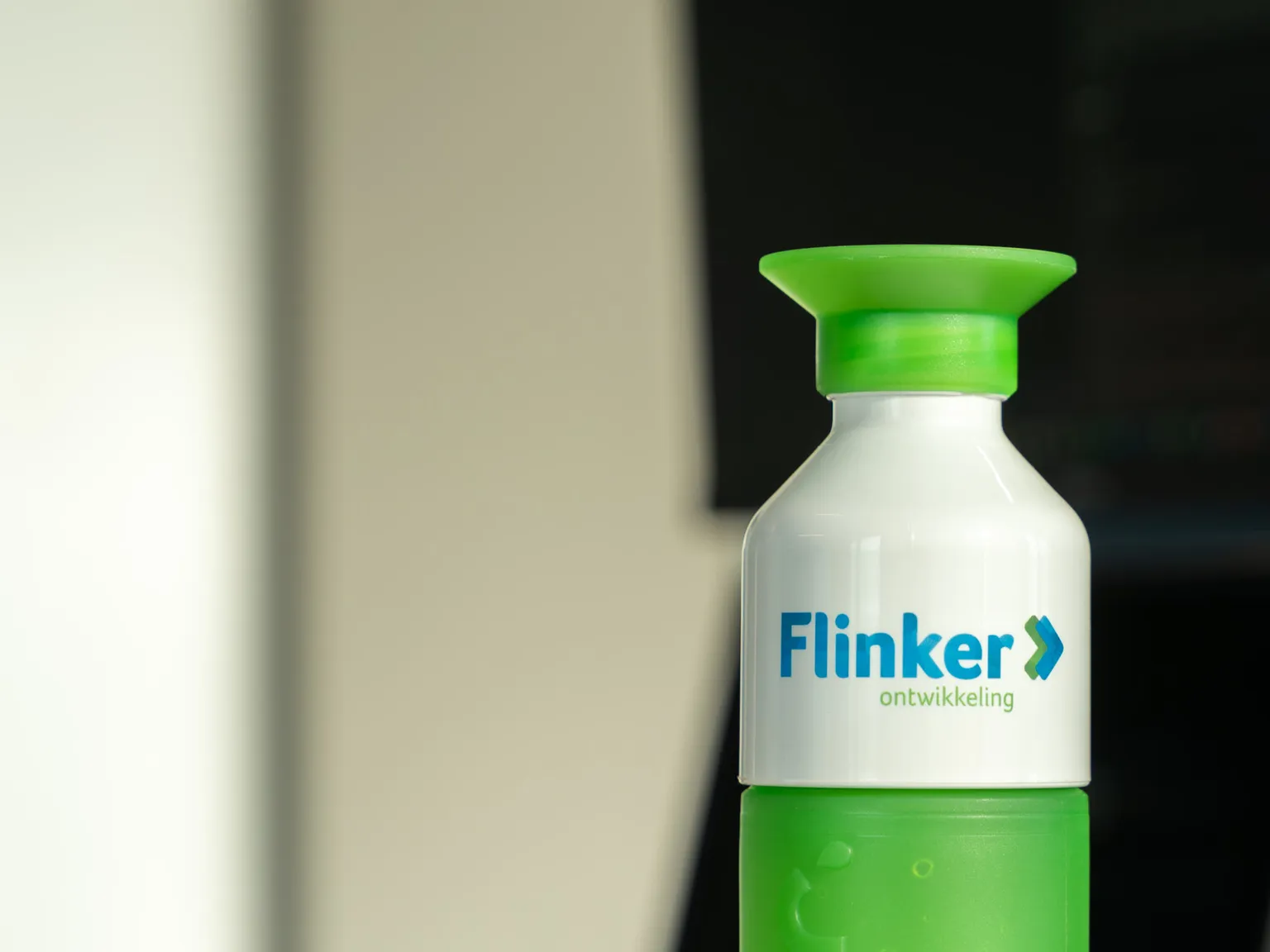 Groene Flinker Ontwikkeling-bidon op een bureau naast een werkende collega