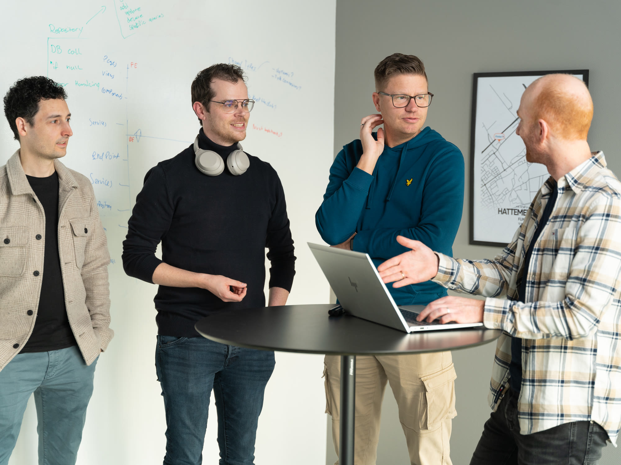 Vier Flinker collega's in gesprek rondom een laptop bij een whiteboard